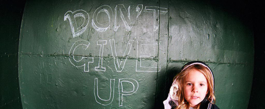 Girl standing next to a wall stating Don't Give Up