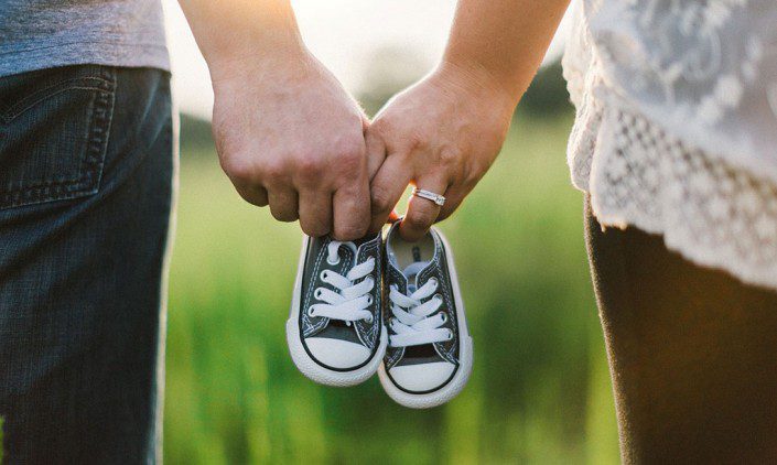 Couple holding hands and a pair of baby shoes