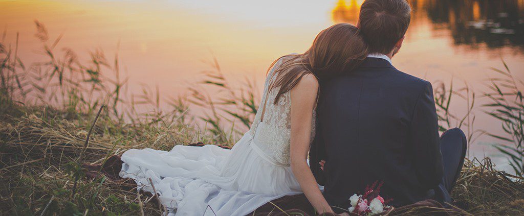 Newly married couple sitting down next to the water