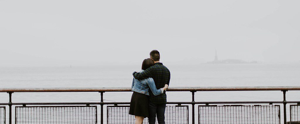 Couple hugging overlooking the water and statue of liberty