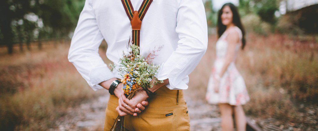 Guy holding flowers behind his back surprising his date