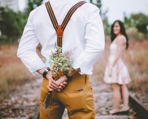 Guy holding flowers behind his back surprising his date