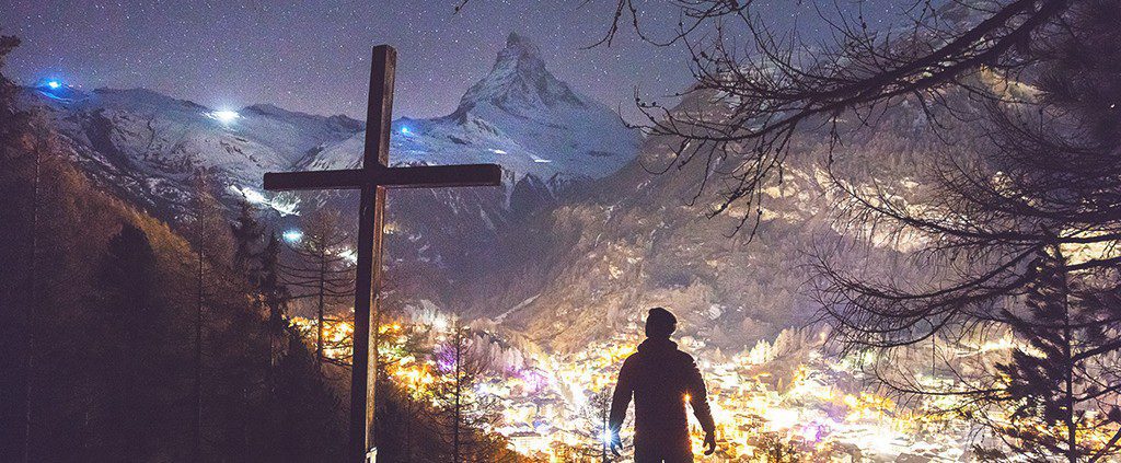 Man standing in the mountains next to a cross
