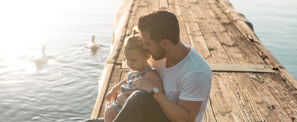 Father sitting on a boardwalk with his daughter looking at ducks
