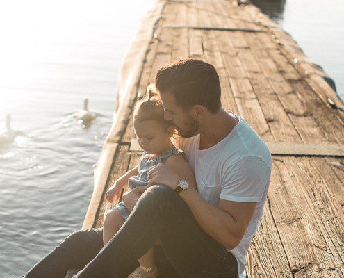 Father sitting on a boardwalk with his daughter looking at ducks