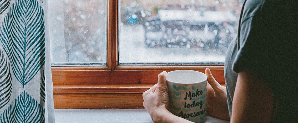 Woman drinking coffee looking at snowfall through the window