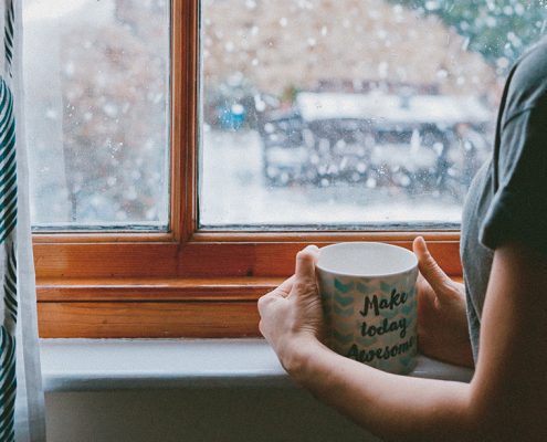 Woman drinking coffee looking at snowfall through the window