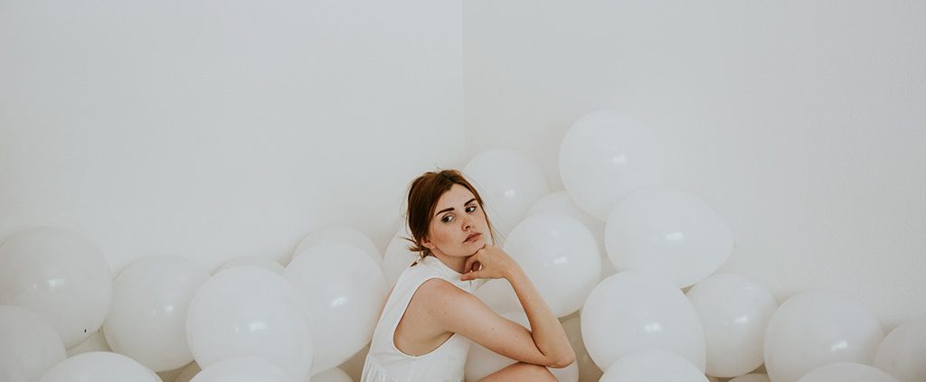 Woman sitting on the floor surrounded by white balloons