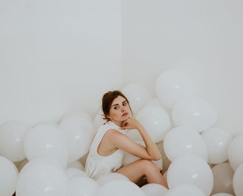 Woman sitting on the floor surrounded by white balloons