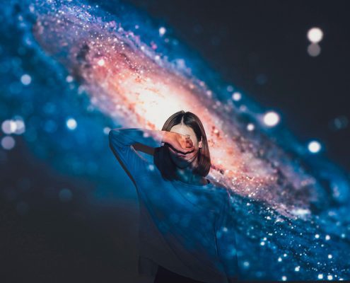 Girl standing in front of a galaxy projector covering her eyes