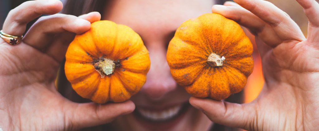 Woman holding miniature pumpkins over her eyes