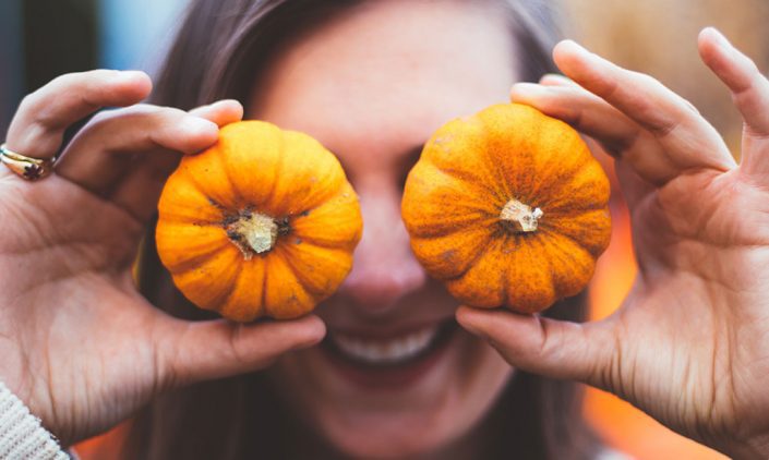 Woman holding miniature pumpkins over her eyes
