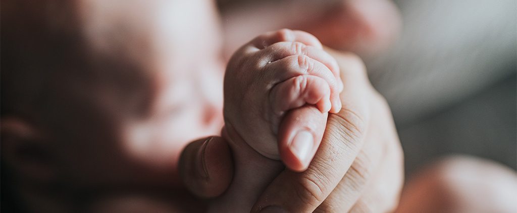 Parent holding the hand of their newborn baby