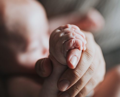 Parent holding the hand of their newborn baby