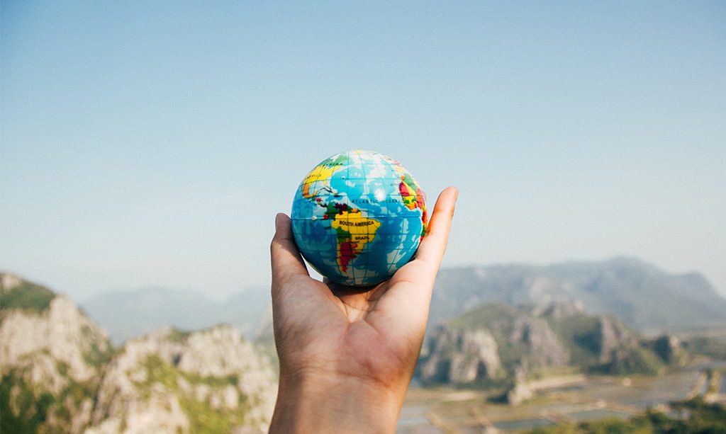 Hand holding a small rubber globe overlooking mountains