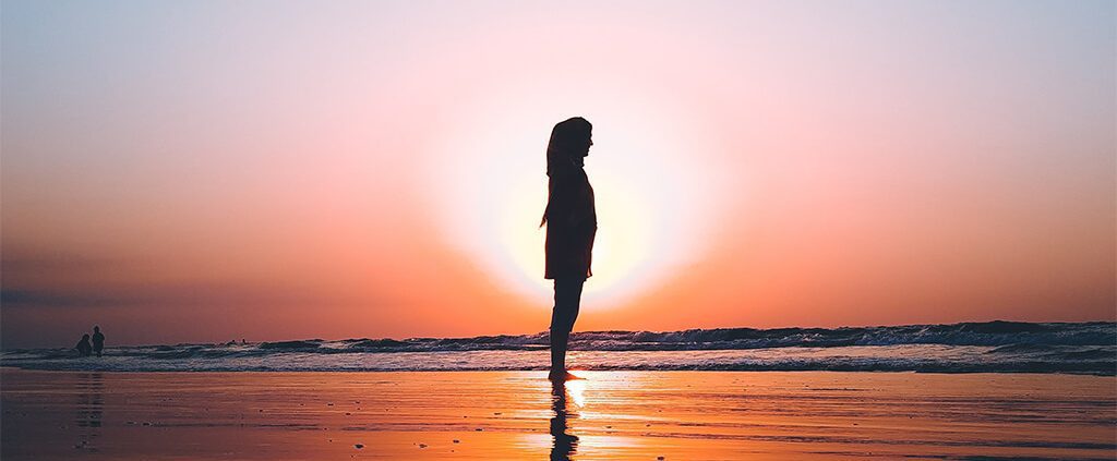 image of lady standing on the beach with sunset behind her