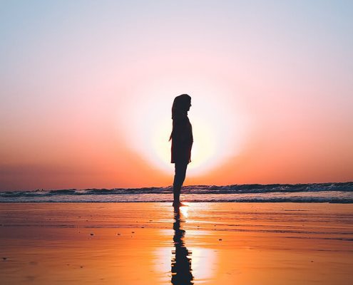 image of lady standing on the beach with sunset behind her