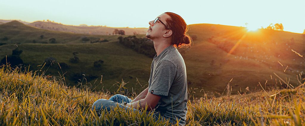 Image of a man sitting on the grass with the sun in the back