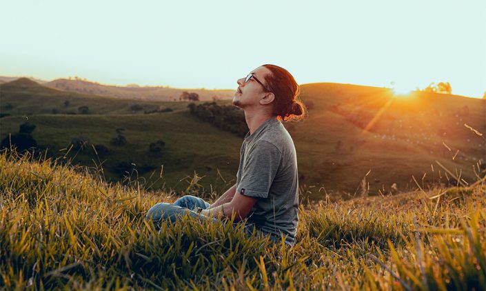 Image of a man sitting on the grass with the sun in the back