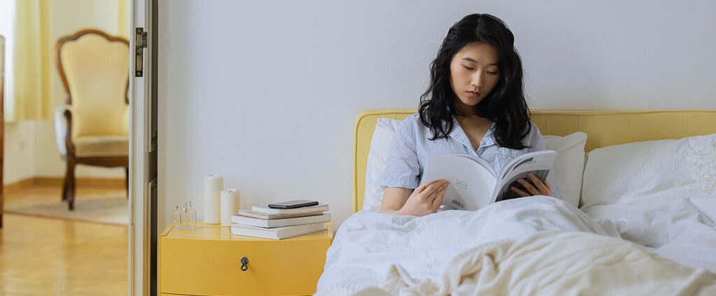 A woman is reading book on her bed