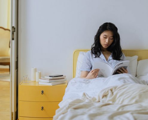 A woman is reading book on her bed