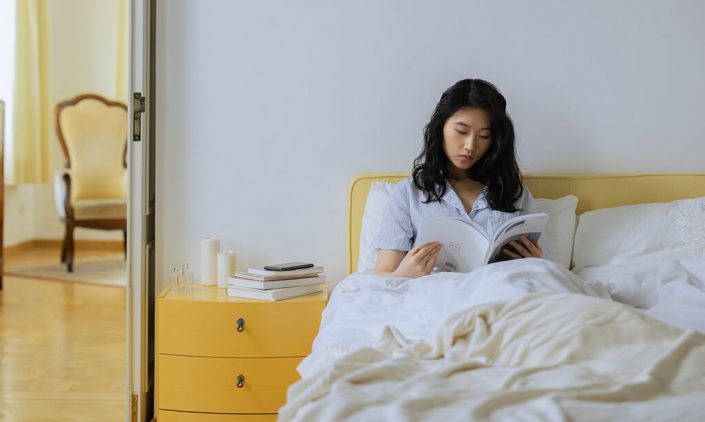 A woman is reading book on her bed