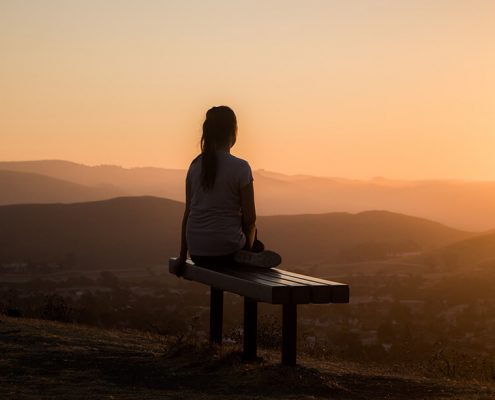 A girl sits on the bench and look at the morning sun