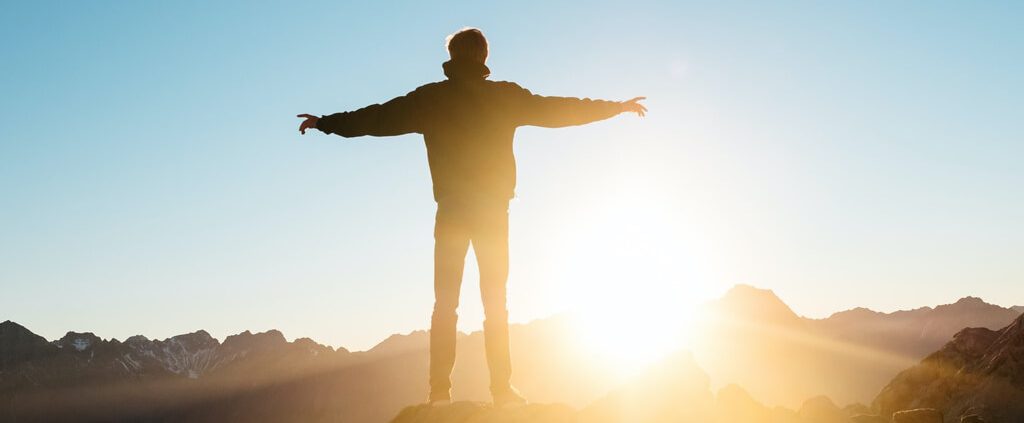 A man standing on top of the hill and welcoming morning sun