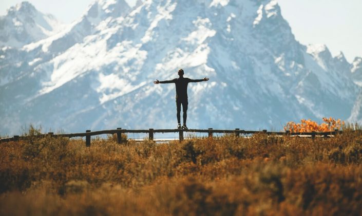 A man is standing on the midst of nature and snowy mountain