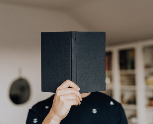 A man uses a book cover his face