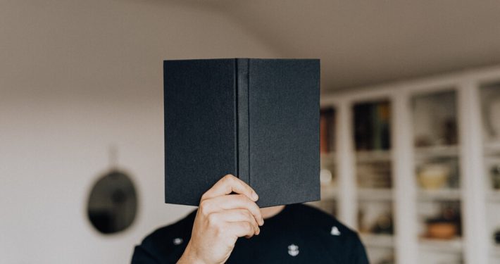 A man uses a book cover his face