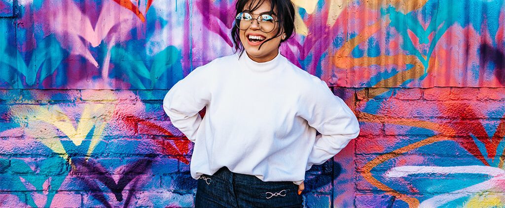 Image of a lady smiling standing against a colourful wall