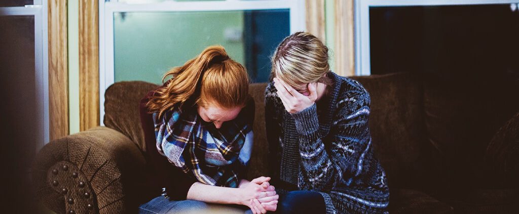 Two women are holding hands and one is crying