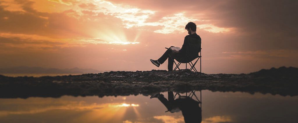 Man reading in nature with view of sunset sky