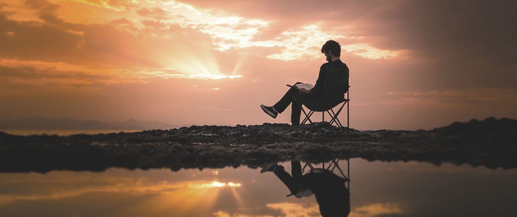 Man reading in nature with view of sunset sky