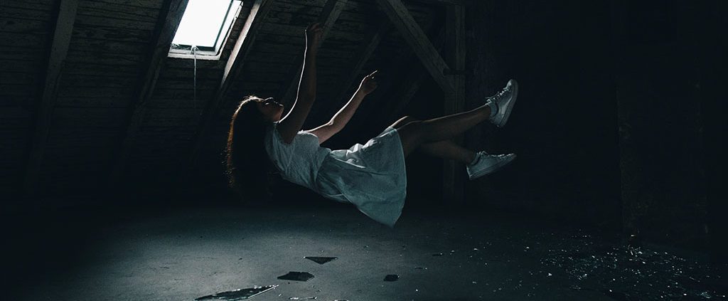 Woman in free-fall position with broken glass underneath.