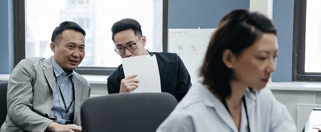 Woman working with gossiping colleagues behind her.