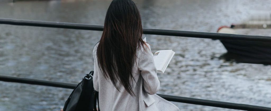 A woman is sitting alone on the riverside and holding a book