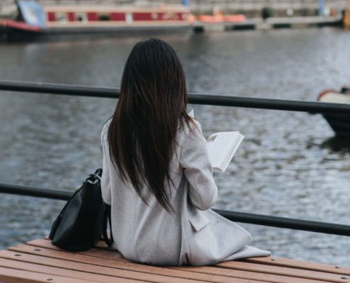 A woman is sitting alone on the riverside and holding a book