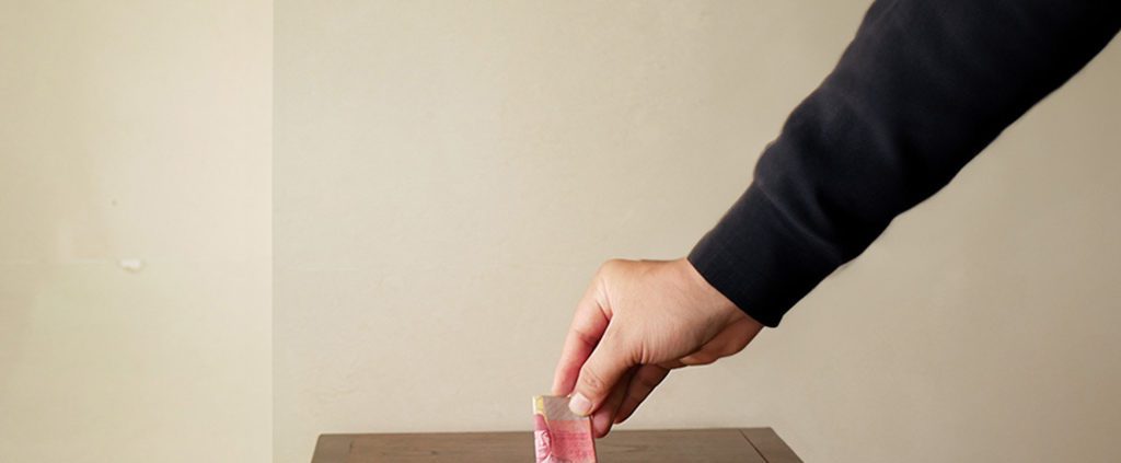 Person's hand putting money into wooden box