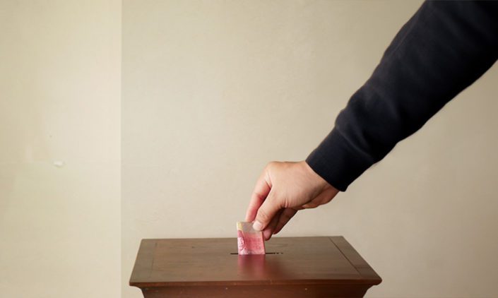 Person's hand putting money into wooden box