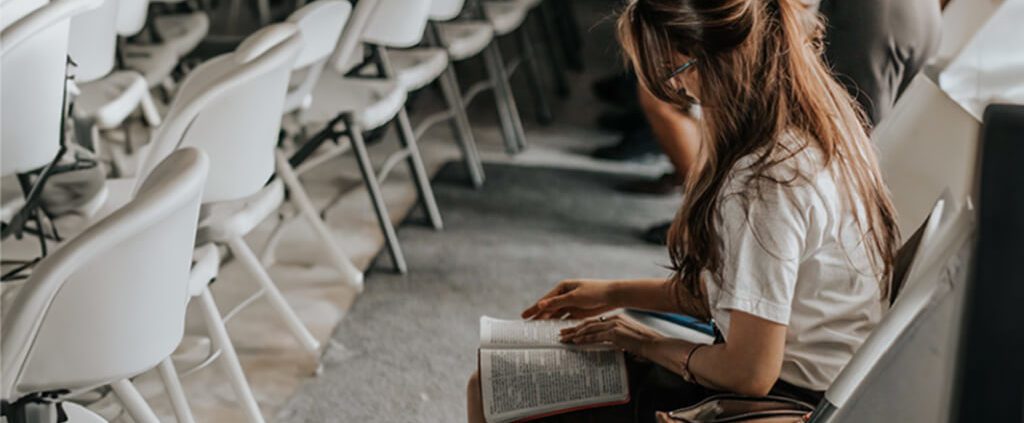 A woman is sitting quietly in the church and reading bible while listening to the sermon