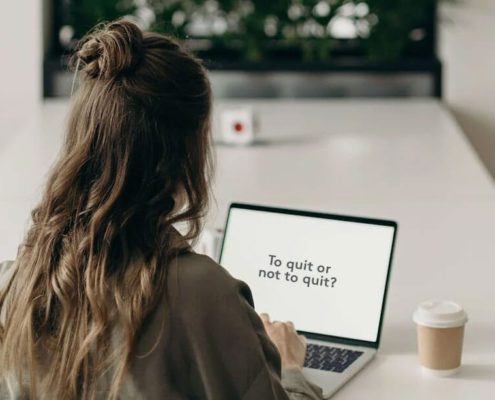 A woman is typing on her laptop "To quit or not to quit?"