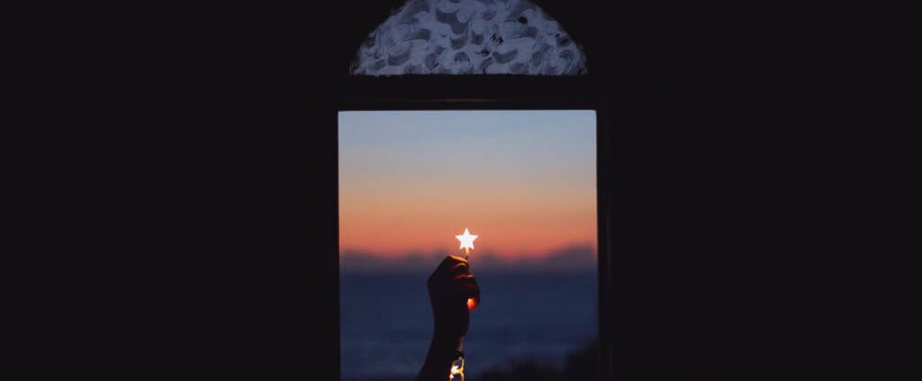 A hand is holding a star light in a window
