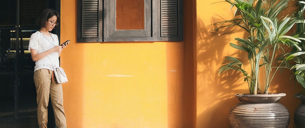 a woman or person waiting in front of a building with yellow wall and plants around her