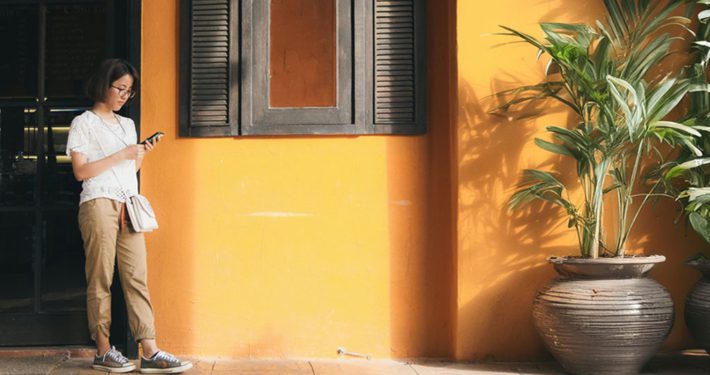 a woman or person waiting in front of a building with yellow wall and plants around her